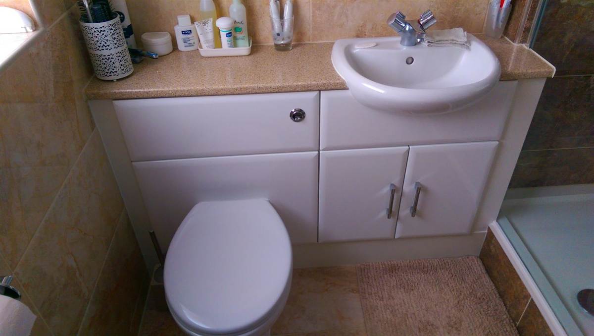 Fitted vanity unit with inset basin, toilet neatly housed underneath, warm-toned tiling throughout