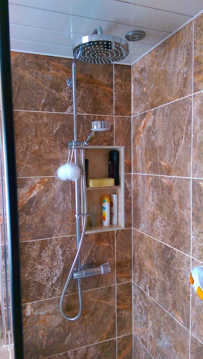 Recessed shower niche built into the tiling — riser rail and rain head above